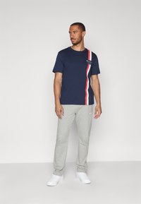 Camiseta de manga corta azul marino con un diseño de rayas verticales rojas y blancas, combinada con pantalones de chándal grises y zapatillas blancas.