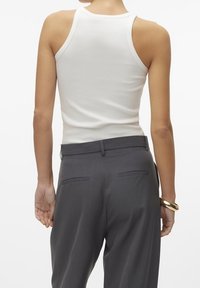 Bílý žebrovaný top na ramínka v kombinaci s tmavě šedými dobře padnoucími kalhotami. Kalhoty mají boční kapsy a hladký, strukturovaný střih.