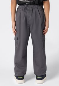 Szare spodnie cargo z elastycznym pasem, bocznymi kieszeniami i prostymi nogawkami. Noszone z granatowymi trampkami z neonowymi akcentami.