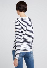 Pull rayé blanc et marine, col rond, manches longues, poignets et ourlet côtelés, associé à un jean bleu, vu de dos.