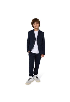 Tumši zils uzvalks ar piegulošu žaketu un atbilstošām biksēm, kopā ar baltu t-kreklu un gaišu sporta apavu pāri. Gluda auduma, moderna piegriezuma.