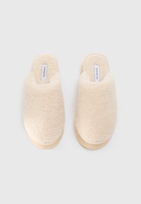 Beige, fluffy tøfler med en bløt tekstur og åpen bakdesign, med en lyse farget såle og en merket innersåle.