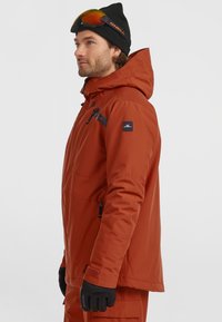 Heren oranje winterjas met een capuchon, zwarte accenten, voorzakken met rits en verstelbare manchetten, gemaakt van een waterdicht materiaal.