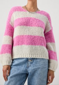 Pull tricoté rayé rose et crème avec manches longues et encolure ronde, présentant une coupe ample et un détail de bord-côte à l'ourlet.