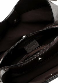 Brown leather handbag interior featuring two zippered compartments and a central section, lined with dark fabric and a magnetic snap closure.