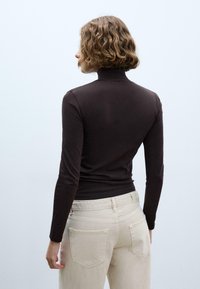 Brązowa, dopasowana koszulka z długim rękawem i golfem, wykonana z gładkiej tkaniny, zestawiona z jasnymi, zwężanymi spodniami.