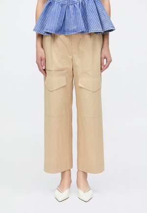 Kvinde iført beige vidde cargo-bukser med klaplommer, en blåstribet peplum-top og hvide slingback-sko med spids tå.