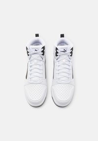 Para białych sneakersów za kostkę z czarnymi akcentami i logo Puma, widziana z góry na jednolitym białym tle.