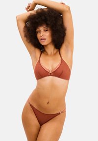 Brun bikini-set med en triangulär topp med en silverfärgad cirkulär detalj och en matchande botten. Slät textur, minimalistisk design och justerbara axelband.