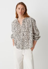 Lightweight, cream blouse with black abstract pattern, collared neckline, long sleeves, and relaxed fit. Button-down front and gathered details.