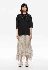 Top negro de gran tamaño con detalles recortados, combinado con una falda asimétrica clara y estampada, y zapatillas plateadas.