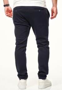 Marineblaue Jogginghosen aus einem weichen, dehnbaren Stoff mit schmal zulaufenden Beinen, ausgestattet mit zwei Rückentaschen mit Knopfverschluss und gerippten Knöchelbündchen.