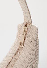 Borsa beige con texture e design a righe, dotata di una cerniera color beige chiaro e una forma strutturata. Manico attaccato per il trasporto.