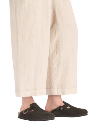 Donkergroene vilten klompen met een ronde neus, gespsaccent en uitsnijdingen, gecombineerd met crèmekleurige wijde pantalons.