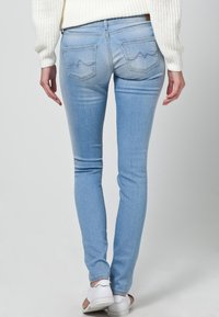 Light blue skinny jeans feature a classic five-pocket design, subtle fading, and curved stitching on the back pockets. Worn with white sneakers.