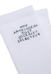 Weiße Baumwollsocken mit schwarzem Text, der "NICHT ANTI-SOZIAL, SONDERN SOZIAL AUSWÄHLEND" in einer fetten Blockschrift zeigt.