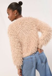 Puhafogú, bézs színű pulóver strukturált felülettel, bordázott mandzsettákkal és kerek nyakkivágással, amit világoskék, bőváló nadrággal párosítottak.