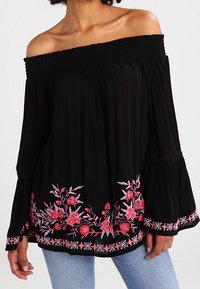 Blusa nera off-the-shoulder con scollatura arricciata, maniche lunghe a campana e ricami floreali colorati all'orlo. Tessuto morbido e leggero.