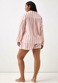 Lätt rosa linne loungewear-set med vita och orangea vertikala ränder; långärmad topp med veck bak och shorts.