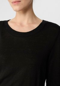 Czarny sweter z dzianiny z okrągłym dekoltem i krótkimi rękawami. Materiał wydaje się miękki i lekki, z lekko teksturowaną powierzchnią.