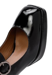 Chaussure plateforme en cuir verni noir avec bout carré, bride à boucle ronde et semelle intérieure texturée marron.