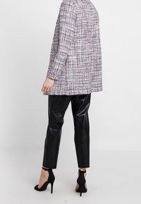 Blazer de tweed rosa claro con texturas variadas, combinado con pantalones de cuero negros. Sandalias negras de tacón alto completan el conjunto.