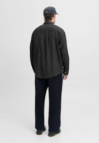 Camisa de cuadros en blanco y negro de manga larga, con puños abotonados, combinada con pantalones oscuros de corte amplio y una gorra azul marino. Diseño sencillo, sin textura.