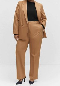 Costume marron ajusté avec un blazer à un bouton et un pantalon droit. Tissu doux et design structuré, associé à un haut noir et des talons foncés.