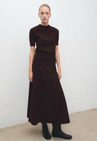 Vestido de punto marrón oscuro con mangas cortas y cuello alto, combinado con botas de tobillo negras ajustadas. Textura suave, diseño de largo completo.
