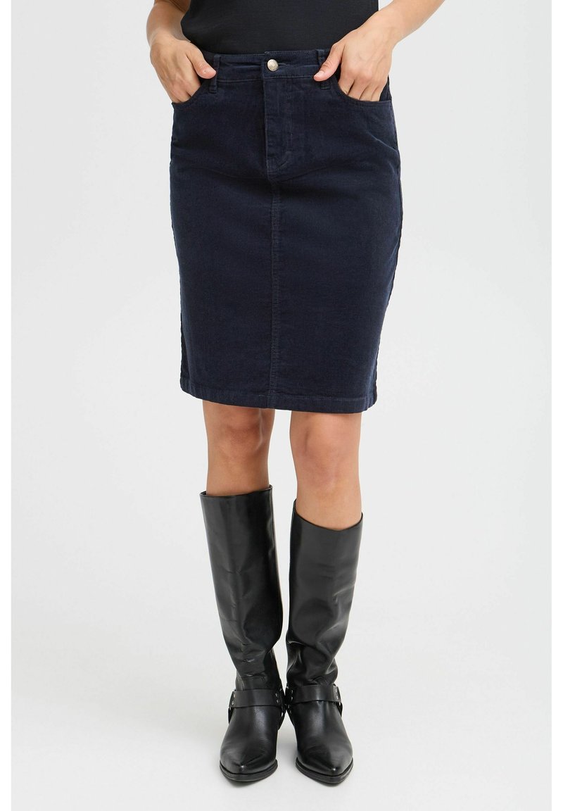 Jupe en denim foncé avec une coupe ajustée, poches avant, et fermeture à un bouton. Associée à des bottes en cuir noir montant jusqu'aux genoux.