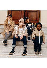 Fyra barn sitter på stentrappor. De har på sig avslappnade vinterkl�äder i neutrala färger, inklusive jackor och kepsar med synliga märkesloggor.