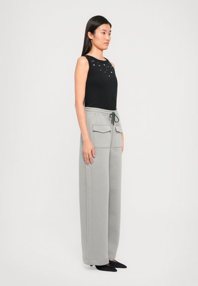 Black sleeveless top with embellishments and gray drawstring pants featuring side pockets, displayed on a model in profile.