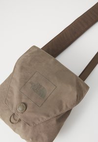 Geantă din material maro pentru umăr cu închidere tip clapă, având un logo debossat, un detaliu cu buton și o suprafață texturată cu model în grilă.