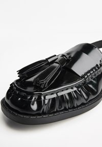 Schwarze Lackleder Slipper mit runder Zehenpartie, ausgestattet mit einer dekorativen Quaste und gerafftem Detail entlang der oberen Kante. Gummisohle.
