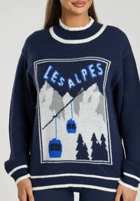 Maglione blu navy con grafica bianca e blu che presenta montagne, alberi e funivie. Collo e polsini a costine, texture morbida, vestibilità rilassata.