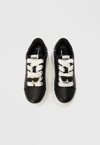 Μαύρα δερμάτινα αθλητικά παπούτσια με άσπρες σόλες. Διαθέτουν άσπρα κορδόνια και διακοσμητικά charms ενός άνδρα και μιας γάτας με γυαλιά ηλίου στα κορδόνια.