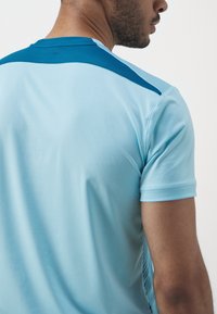 Světle modré sportovní tričko s texturovaným tmavě modrým ramenním panelem a krátkými rukávy, navržené pro pohodlí a výkon.