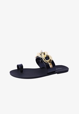 Sandalia plana negra con acento floral dorado, hecha de material brillante. Cuenta con un bucle para el dedo del pie y una suela suave. Diseño minimalista.