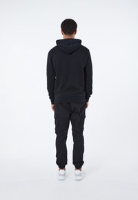 Sudadera negra con capucha ajustable, combinada con pantalones cargo negros que tienen bolsillos laterales, y zapatillas blancas. Tela suave.