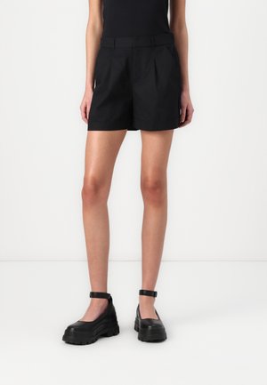 Sorte skreddersydde shorts med frontfolder, sidelommer og en flat midje. Kombinert med chunky sorte platåsko med ankelstropper.
