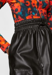 Färgglad långärmad topp med ett abstrakt mönster i rött, blått och svart, kombinerad med svarta lädershorts med elastisk midja och sidficka.