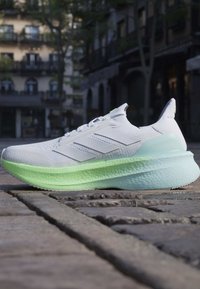 Chaussure de sport blanche et vert clair avec une semelle épaisse placée sur une rue pavée dans un environnement urbain extérieur.