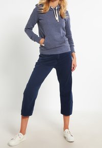 Mörkblå bomullshoodie med dragsko, framficka och långa ärmar, parat med beskurna mörkblå byxor och vita sneakers.