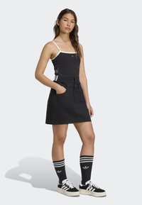 Černý tílko s krémovými ramínky, spárované s černou džínovou sukní s kapsami a postranními pruhy. Černobílé pruhované ponožky a tenisky.