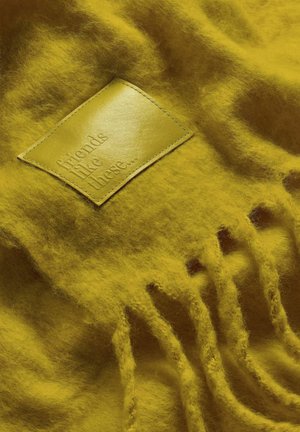 Žuta vunena šal s kožnom etiketom s reljefnim natpisom "prijatelji poput ovih..." i resicama sa jedne strane.