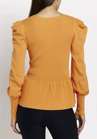 Maglione arancione a coste con maniche lunghe e gonfiate e orlo peplum svasato. La parte posteriore presenta un collo rotondo e un tessuto testurizzato.
