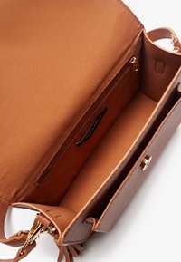 Brown synthetic handbag with a smooth texture, featuring a spacious interior, a zippered pocket, and gold hardware accents.