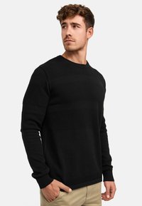 Musta neulepaita, jossa on kohokuvioidut raidat, pyöreä kaula-aukko ja istuvat hihansuut. Tyylikäs muotoilu sileällä kangaspinnalla.