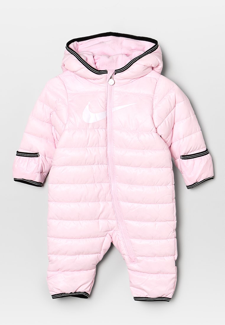 Un traje de nieve puffy de color rosa bebé con cremallera frontal, capucha y ribetes negros en las mangas, que presenta un logo blanco de Nike en el pecho.