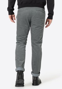 Grijze corduroy broek met een taps toelopend ontwerp, voorzien van opgerolde mouwen, twee achterzakken en een gestructureerde stof. Gemaakt met zwarte laarzen.